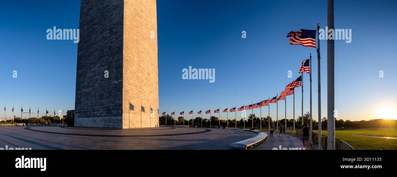 Monumento a Washington con bandiere americane al tramonto Washington DC // WASHINGTON DC - il monumento a Washington, un obelisco di spicco che commemora George Washington, è affiancato da un semicerchio di 50 bandiere americane al tramonto. Questo punto di riferimento nazionale sul National Mall è costruito principalmente in marmo, granito e gneiss di pietra blu. Con un'altezza di 555 piedi e 1/8 pollici (169,29 metri), è la struttura in pietra e l'obelisco più alti del mondo, con una costruzione dal 1848 al 1884. Il basso sole tramonta proietta lunghe ombre dei flagpali attraverso il monumento e la piazza circostante. Foto Stock