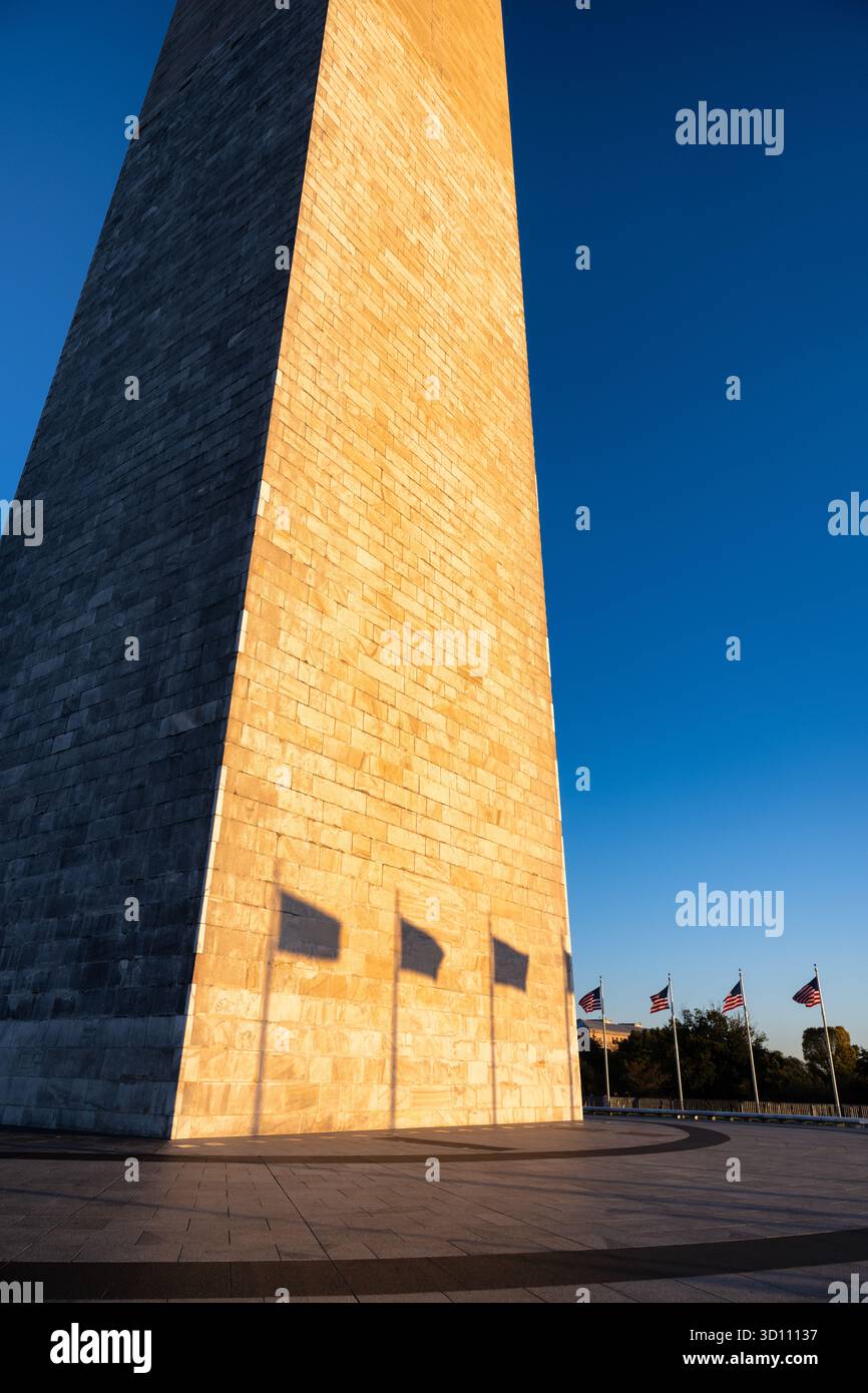Monumento a Washington con le ombre della bandiera al tramonto Washington DC // WASHINGTON DC - il monumento a Washington è illuminato dal sole che tramonta, proiettando ombre delle bandiere circostanti e assumendo un bagliore dorato. Questo iconico obelisco, un monumento a George Washington, è la struttura in pietra più alta del mondo e l'obelisco più alto, alto 169,29 metri (555 piedi e 1/8 pollici). Situato sul National Mall, è costruito in marmo, granito e gneiss di pietra blu. Cinquanta bandiere americane circondano la sua base, rappresentando gli stati Uniti. Foto Stock