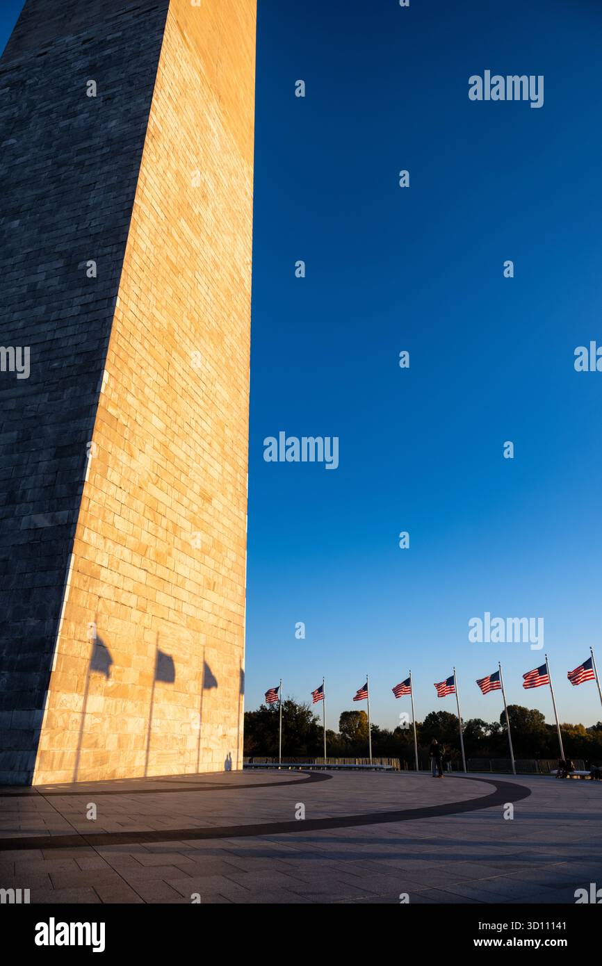 Monumento a Washington con le bandiere e il tramonto Glow Washington DC // WASHINGTON DC - il monumento a Washington è illuminato dal sole che tramonta, gettando ombre delle bandiere circostanti. Questo iconico obelisco, in onore del primo presidente degli Stati Uniti George Washington, è una caratteristica importante del National Mall. Costruito principalmente in marmo, granito e gneiss di pietra blusica, è la struttura e obelisco in pietra più alti del mondo, con un'altezza di 169,29 metri (555 piedi e 1/8 pollici). Il bagliore dorato del monumento al tramonto mette in risalto la sua complessa lavorazione in pietra e il suo significato storico, fungendo da potente simbo Foto Stock