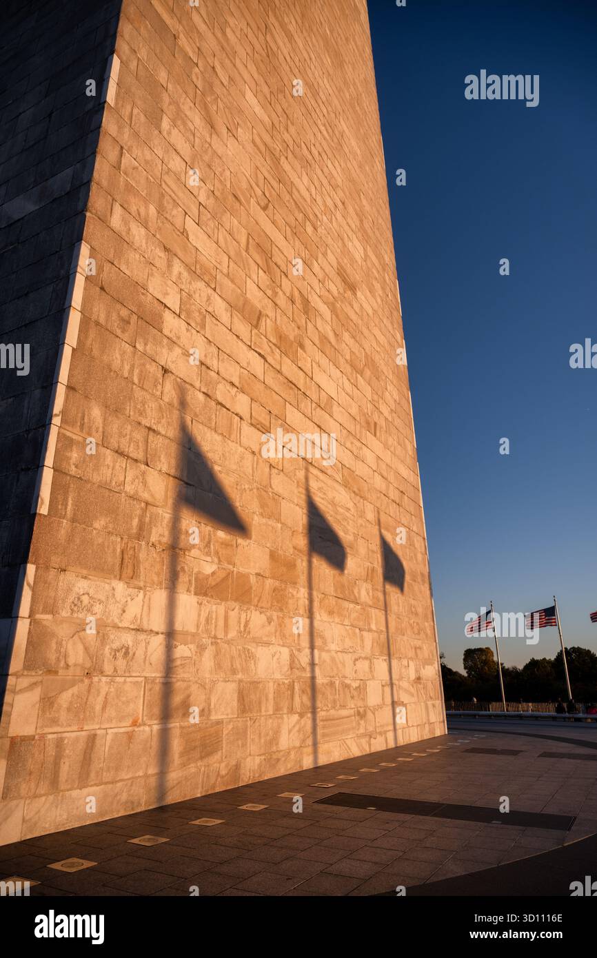 Monumento a Washington con le ombre della bandiera al tramonto Washington DC // WASHINGTON DC - il monumento a Washington è illuminato dal sole che tramonta, proiettando ombre prominenti delle bandiere americane sulla sua facciata in pietra. Il basso sole all'orizzonte crea un bagliore dorato sulla superficie del monumento. Questo iconico obelisco, dedicato a George Washington, è la struttura in pietra più alta del mondo e l'obelisco più alto, raggiungendo i 169,29 metri (555 piedi e 1/8 pollici). Costruito in marmo, granito e gneiss di pietra tra il 1848 e il 1884, è un punto di riferimento centrale del National Mall. Foto Stock