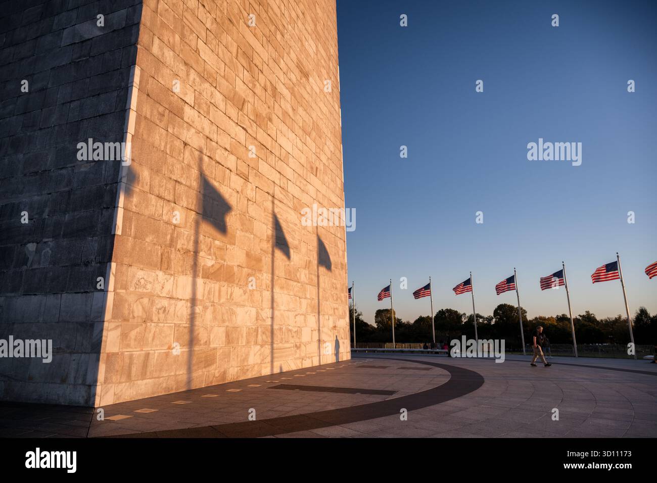 Monumento a Washington con le ombre della bandiera al tramonto Washington DC // WASHINGTON DC - il monumento a Washington è illuminato dal sole che tramonta, gettando ombre delle bandiere americane sulla sua pietra dalle tonalità dorate. Questo obelisco onora George Washington, il primo presidente degli Stati Uniti. Situato sul National Mall, il monumento è un importante punto di riferimento nella capitale della nazione, costruito principalmente in marmo, granito e gneiss di pietra blu. Con un'altezza di 169,29 metri (555 piedi 5 1/8 pollici), fu completata nel 1884. Foto Stock
