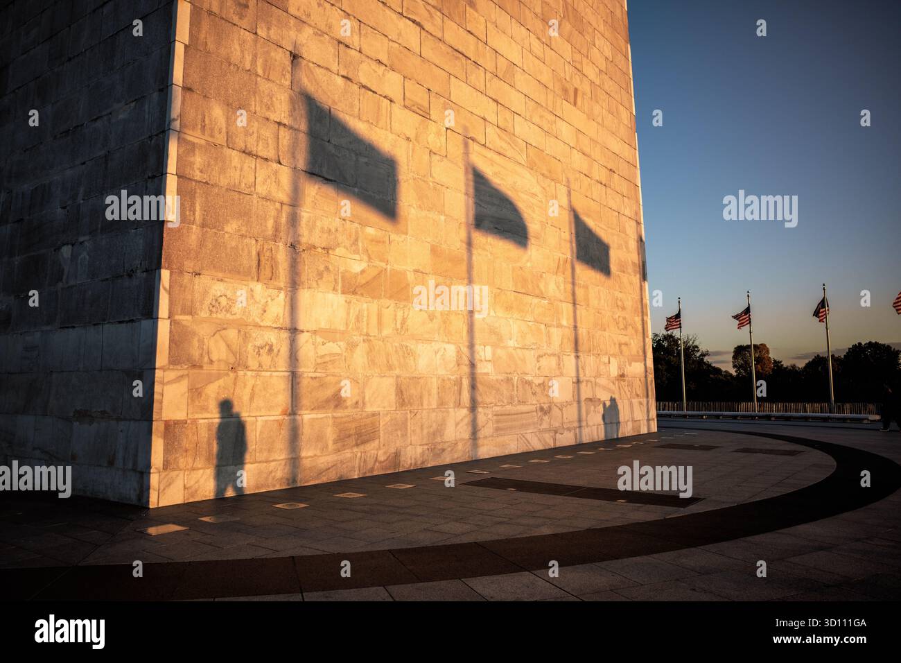 Monumento a Washington al tramonto Washington DC // WASHINGTON DC - il monumento a Washington è illuminato dal sole del tardo pomeriggio, gettando lunghe ombre delle bandiere americane e dei visitatori sulla sua facciata in marmo, granito e gneiss di pietra blu. Questo iconico obelisco onora George Washington, il primo presidente degli Stati Uniti. Completato nel 1884, si trova sul National Mall ed è alto 169,294 metri (555 piedi e 1/8 pollici). Un anello di 50 bandiere americane circonda permanentemente il monumento, rappresentando gli stati statunitensi. Foto Stock
