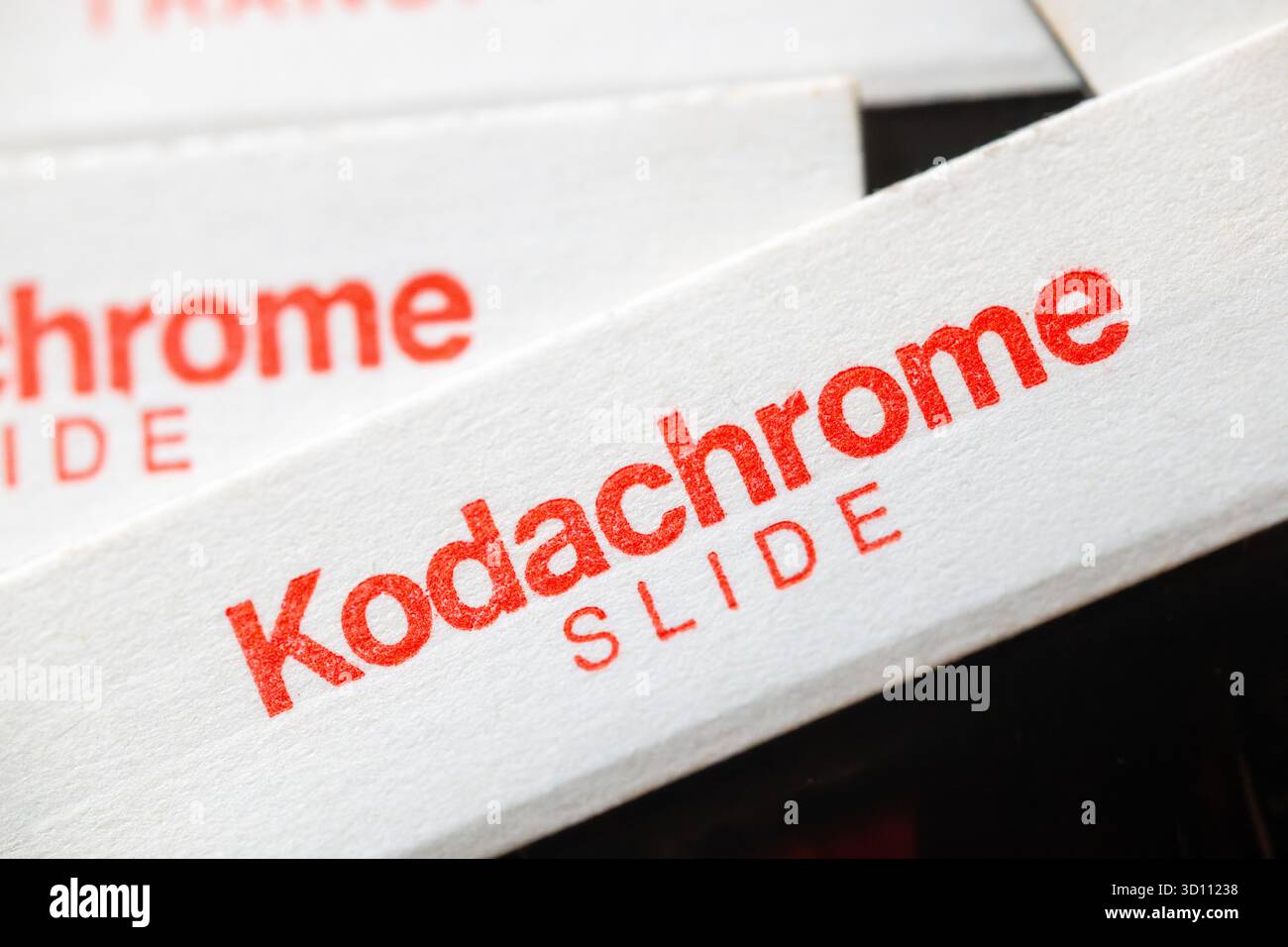 La vista ravvicinata di uno scivolo Kodachrome rivela la sua caratteristica scritta rossa su un supporto in cartone bianco. Kodachrome, introdotto da Eastman Kodak nel 1935, è stato celebrato per la sua eccezionale stabilità di archiviazione, nitidezza e vivaci rendering dei colori, rendendolo uno dei preferiti per decenni dai fotografi. La produzione di questo iconico film cessò nel 2009, con l'ultimo laboratorio di lavorazione che terminò nel 2010, segnando la fine di un'era significativa nella fotografia analogica. Foto Stock