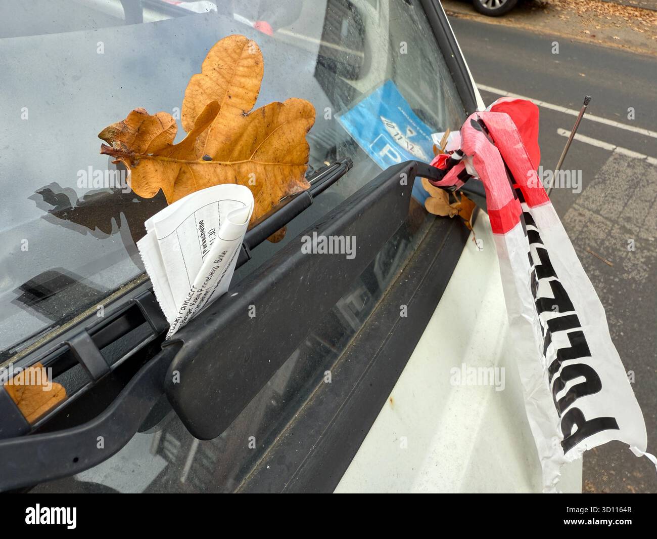 Una cassetta della polizia e un biglietto per il parcheggio attaccati al parabrezza di un'auto con foglie autunnali. Concetto per le forze dell'ordine multe per il controllo stradale e la città di tutti i giorni l Foto Stock