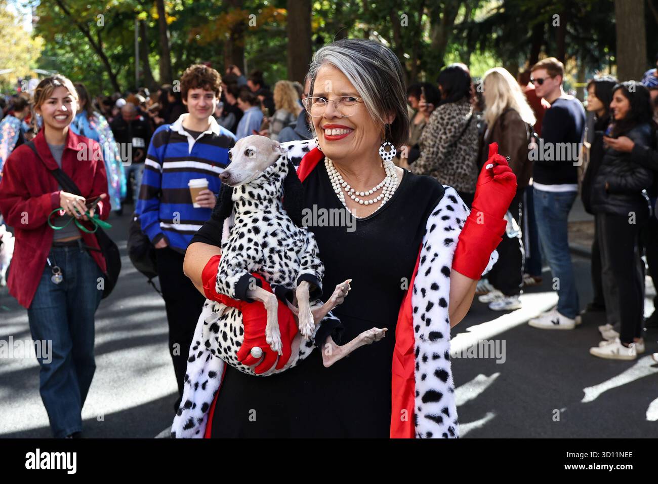 Una donna vestita da Cruella De Vil porta il suo cane in posa per una foto durante la sfilata dei cani di Halloween del Washington Square Park a New York City sabato 25 ottobre 2025. (Foto: Gordon Donovan) Foto Stock