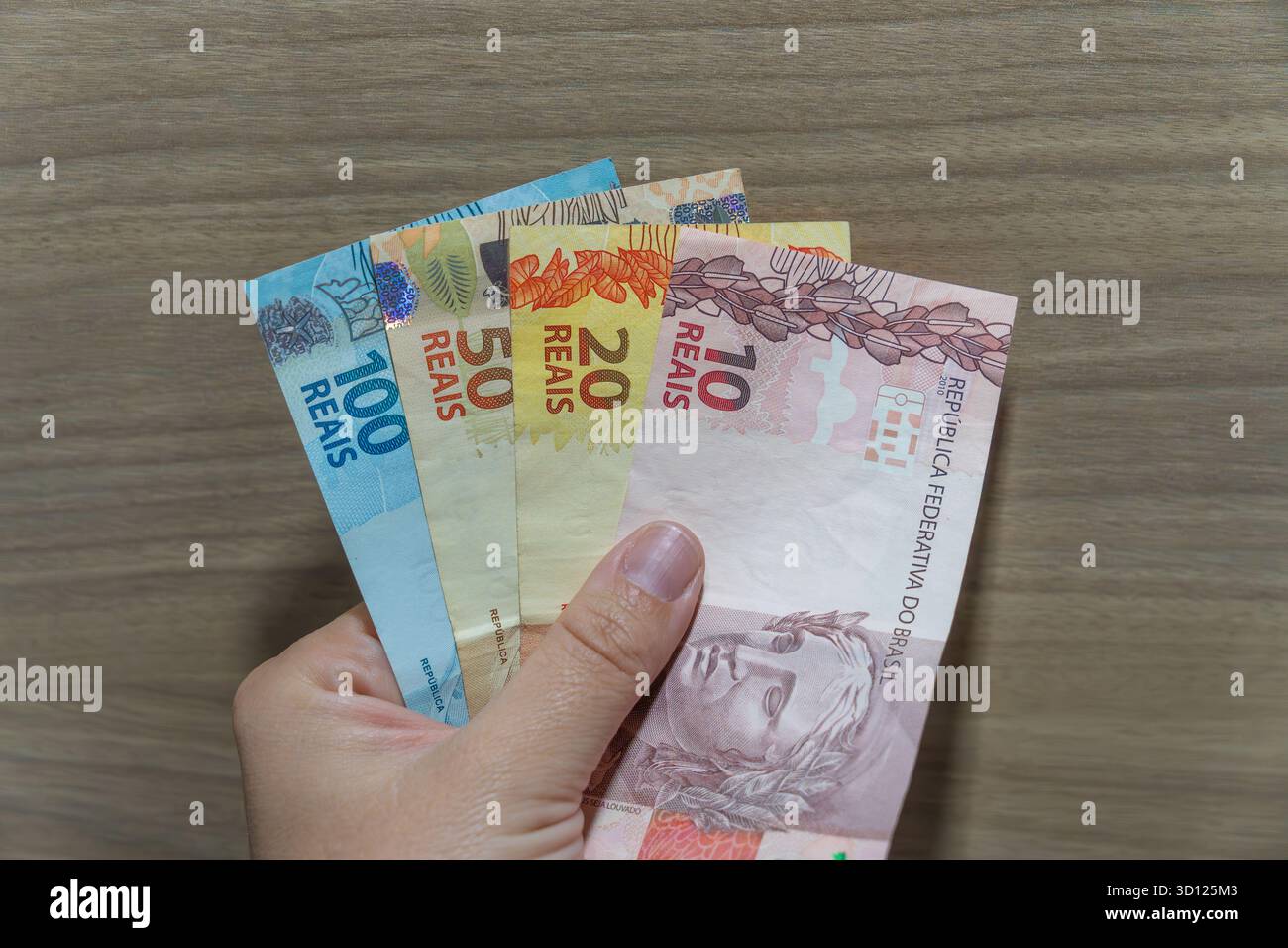 Mano che tiene in mano banconote brasiliane, mostrando vari tagli per i concetti di finanza, pagamento ed economia Foto Stock