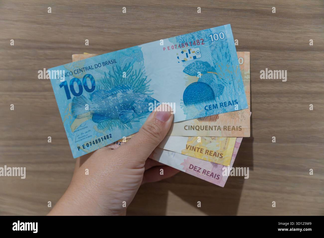donna che afferra a mano un fascio di note brasiliane colorate, tra cui 100, 50, 20 e 10 reais, illustrare le transazioni finanziarie Foto Stock