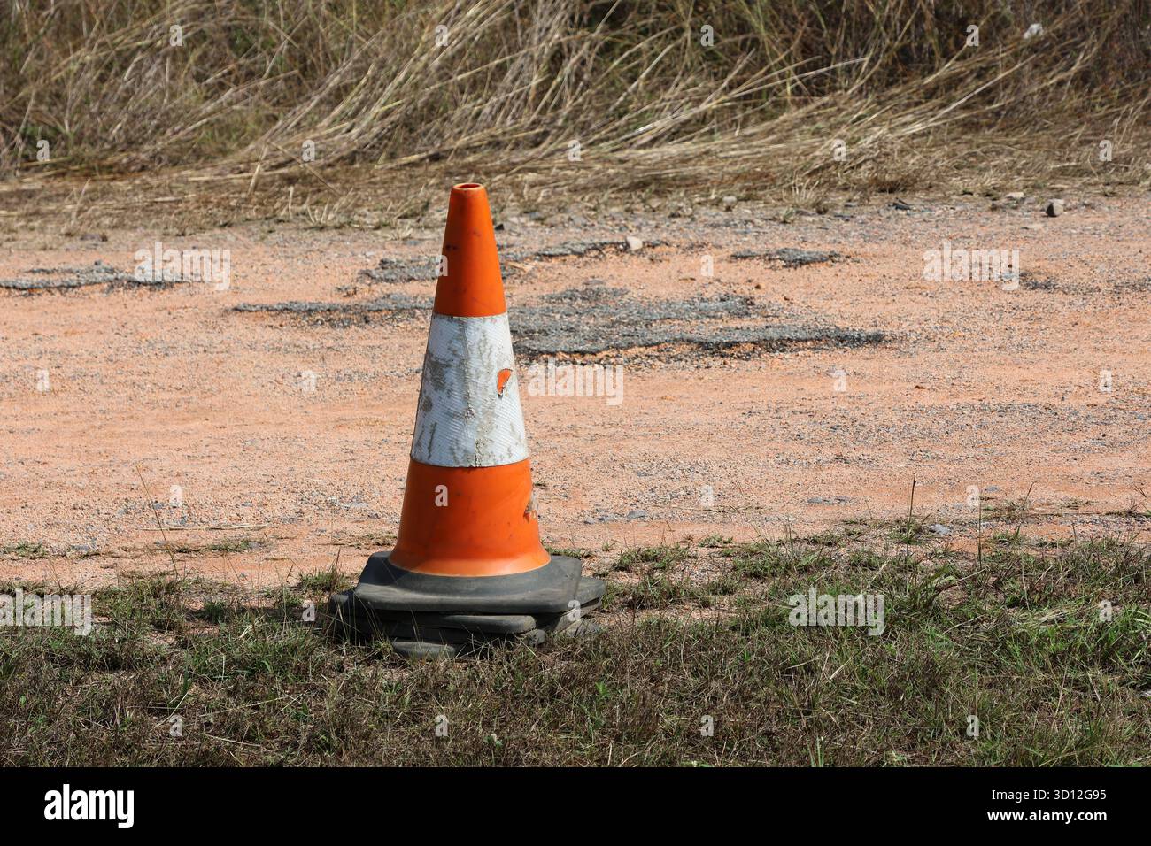 Vecchio cono stradale arancione e bianco intemprato su erba e ghiaia Foto Stock