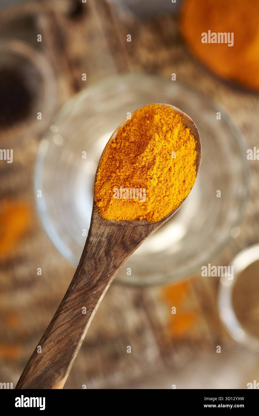 Polvere di radice di curcuma essiccata su un cucchiaio sopra un bicchiere d'acqua, con pepe nero macinato sullo sfondo, vista dall'alto Foto Stock