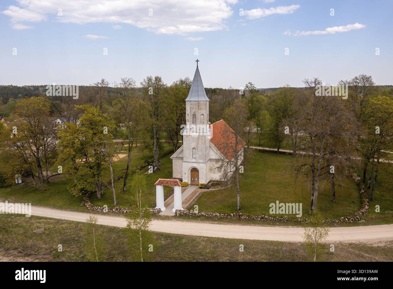 Una pittoresca chiesa sorge da sola in un vivace paesaggio verde circondato da alberi e sentieri, renda, Lettonia Foto Stock