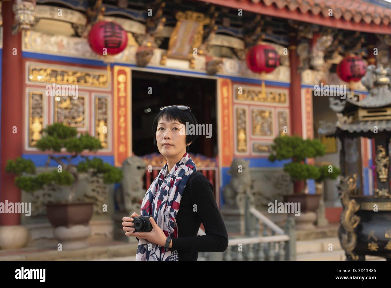 Una moderna donna asiatica tiene in mano una macchina fotografica che viaggia in un vecchio edificio cinese Foto Stock