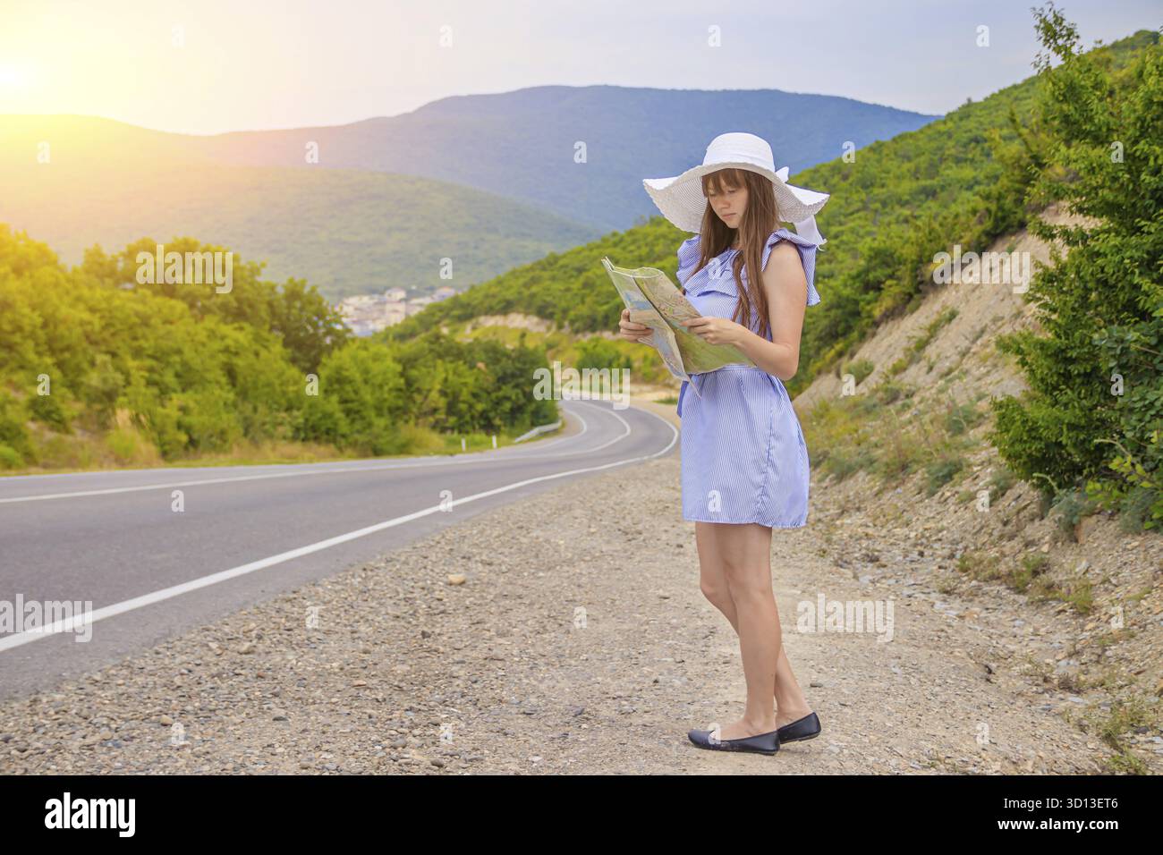 La ragazza con la mappa sta cercando la strada. Una bella ragazza sta cercando un percorso. Strada in montagna. La ragazza nel cappello. Articolo sul ciao Foto Stock