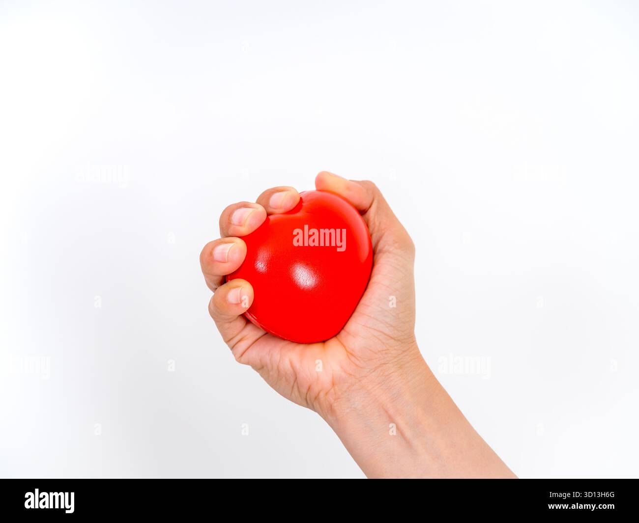 Mano che stringe una palla di stress a forma di cuore rossa, simboleggia la salute del cuore, il monitoraggio della pressione sanguigna, sollievo dallo stress, cure cardiovascolari, e noi medici Foto Stock