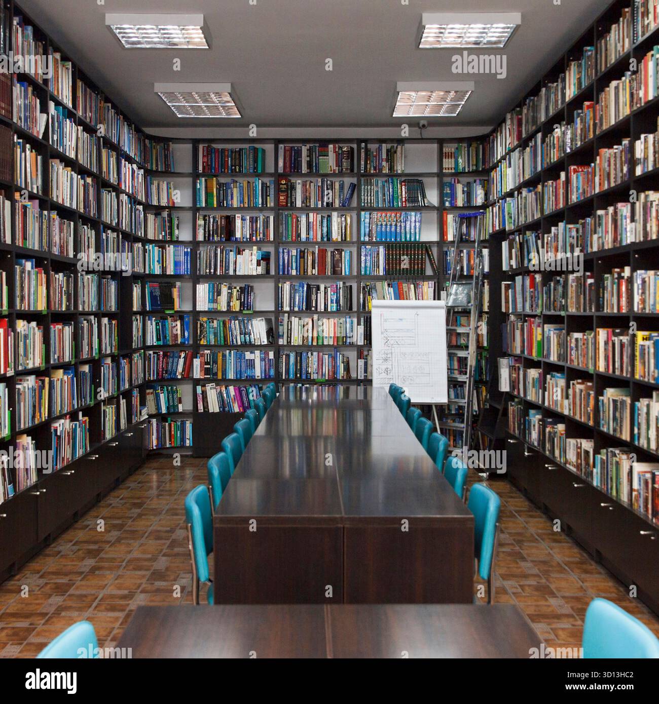 CHISINAU, MOLDAVIA - 14 MARZO 2025; interno della biblioteca con lunghi tavoli in legno, sedie blu e scaffali pieni di libri su pavimento piastrellato, che simboleggiano educa Foto Stock