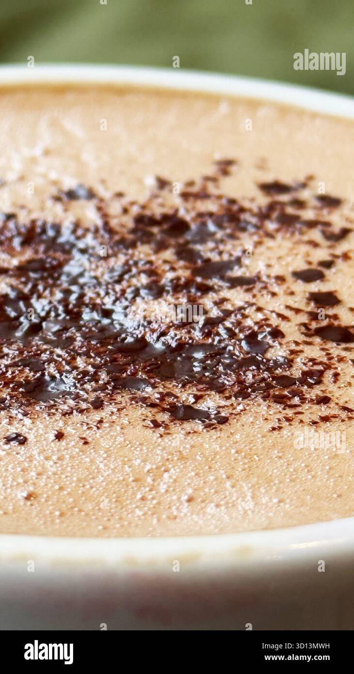 Bevanda con cioccolata calda con cacao in polvere spolverato in tazza in ceramica, dettaglio ravvicinato della consistenza cremosa. Foto mobile Foto Stock
