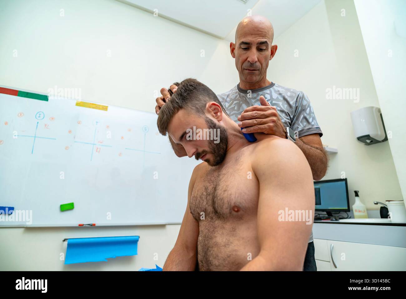 Fisioterapista che esegue la mobilizzazione dei tessuti molli assistita dallo strumento sul collo di un cliente Foto Stock