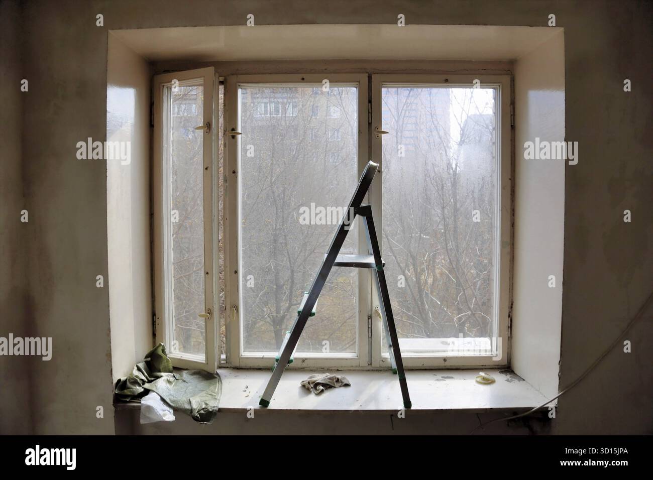 Piccola scala a cavalletto in alluminio in piedi davanti alla vecchia finestra della stanza Foto Stock