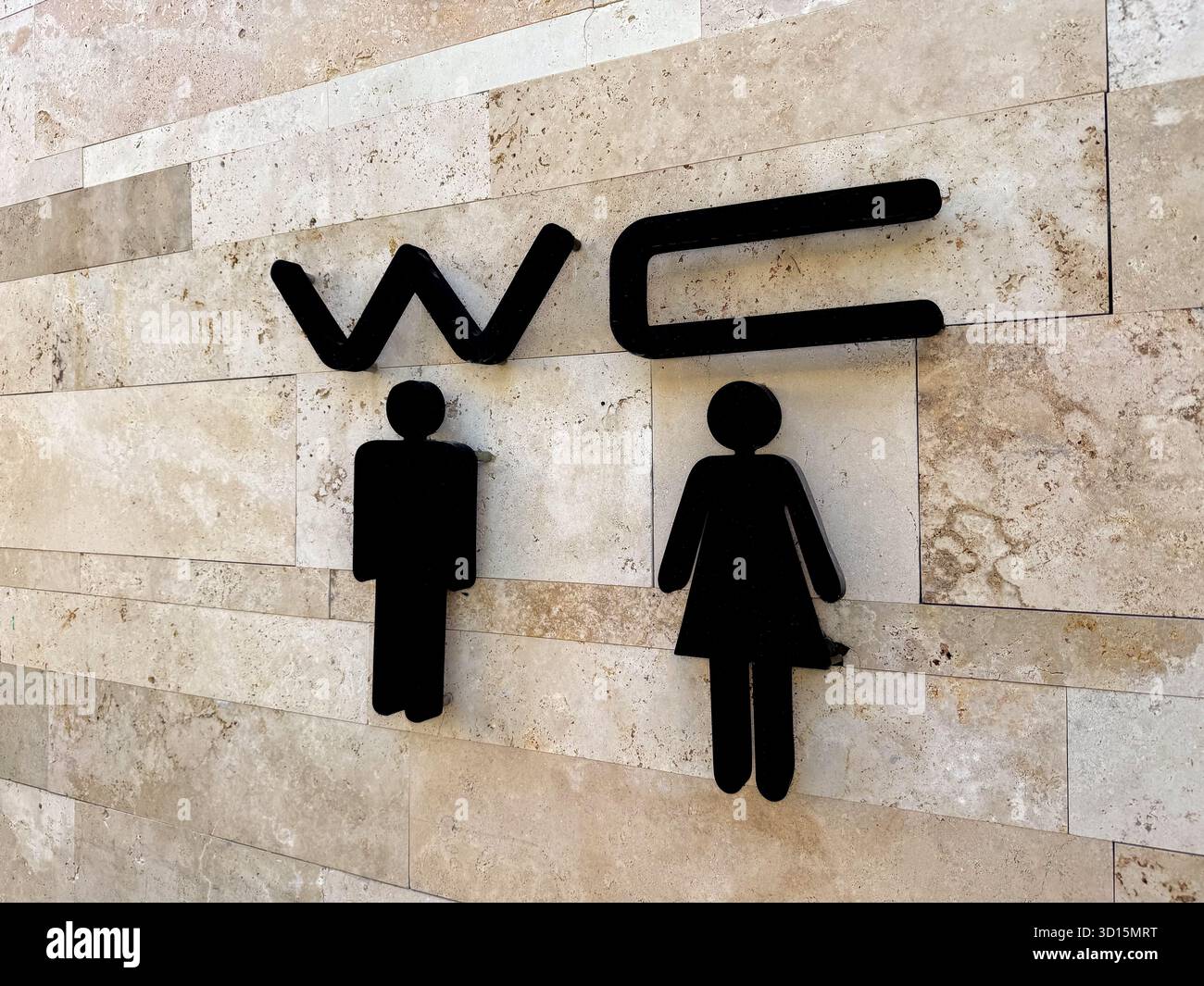 Cartello per i servizi igienici su un muro di pietra. Il cartello presenta simboli maschili e femminili in nero, che indicano la posizione dei bagni per uomini e donne. Foto Stock