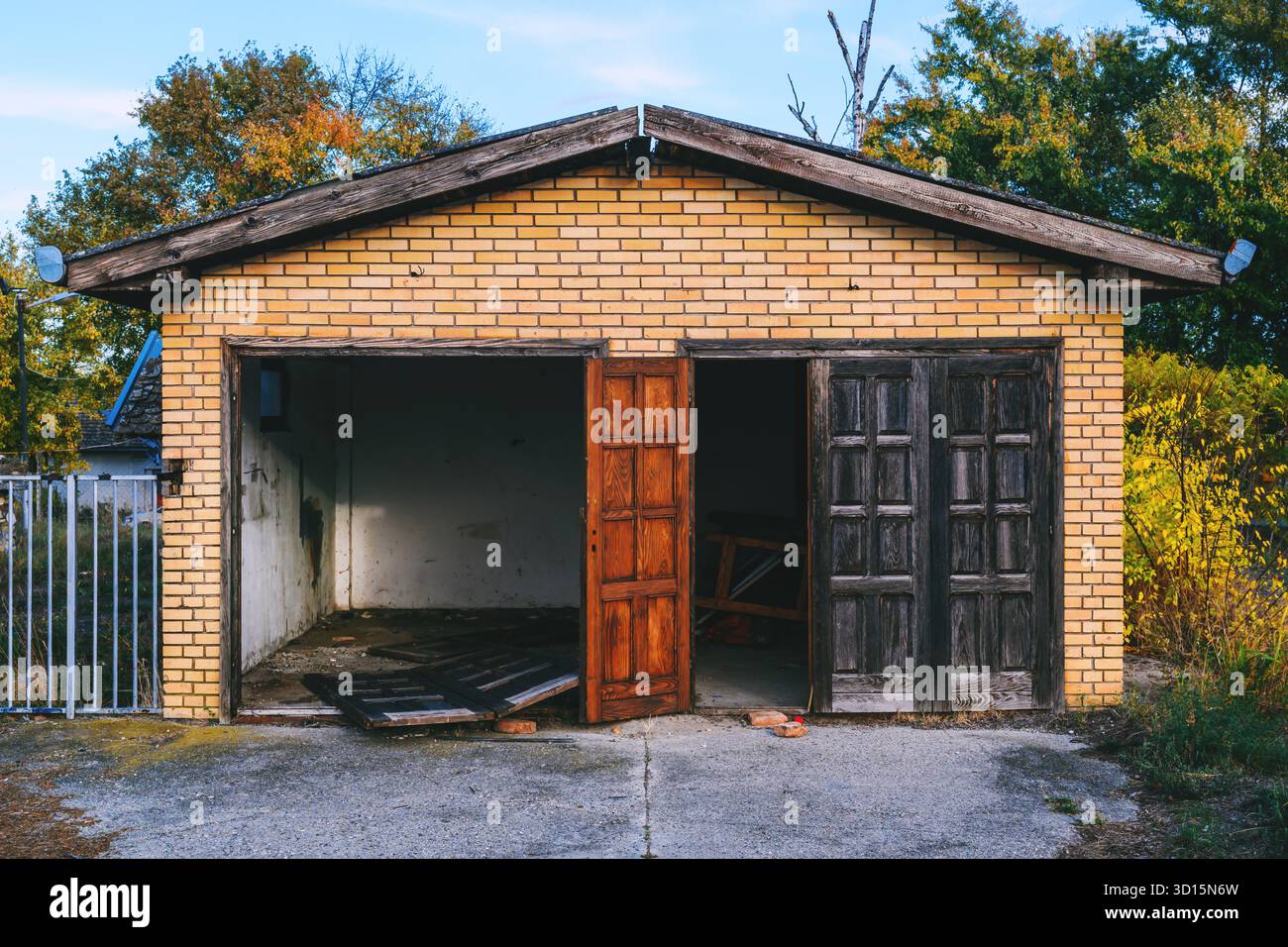 Vecchio garage abbandonato con pareti in mattoni incrinati e due porte in legno intemperie in decadenza, che mostravano negligenza e deterioramento. Messa a fuoco selettiva. Foto Stock