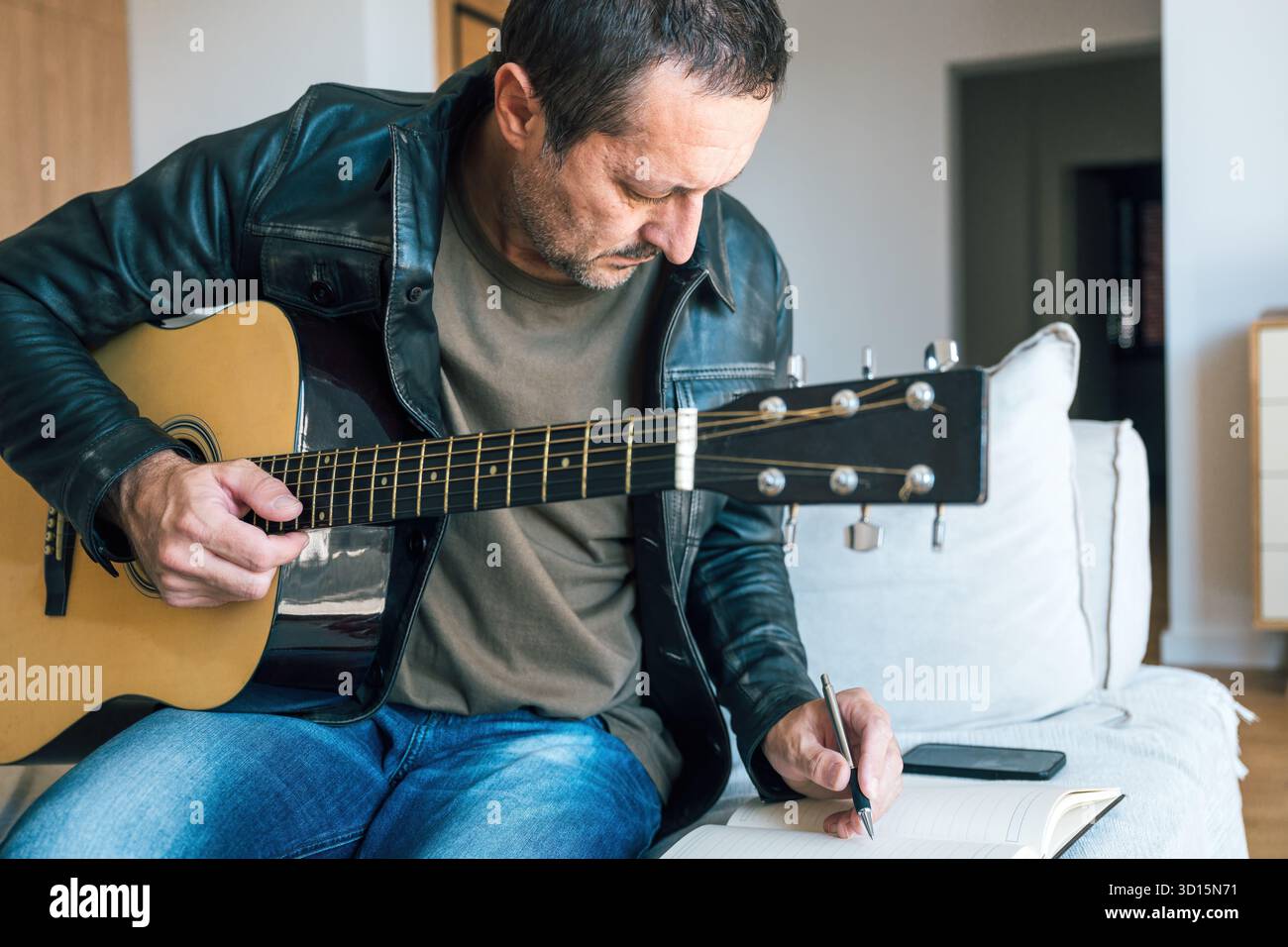 Uomo maturo a casa che suona la chitarra acustica e scrive testi su notebook, concetto di creatività, scrittura di canzoni e ispirazione artistica in Everyday li Foto Stock