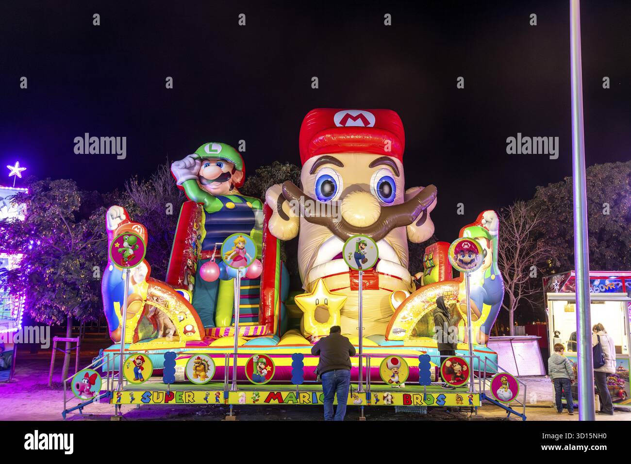 Barcellona, Catalogna - Spagna - 01-07-2025: Grande castello gonfiabile a tema Mario e Luigi con colori neon luminosi di notte, circondato da persone Foto Stock