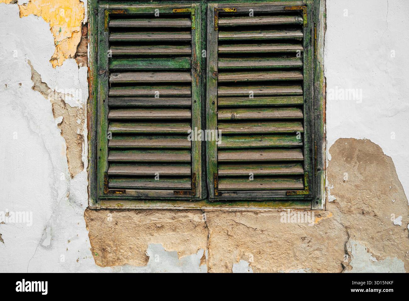 Vecchia finestra in legno con persiane veneziane su un muro incrinato in rovina, simbolo del decadimento e del passaggio del tempo, texture e dettagli architettonici vintage. Foto Stock