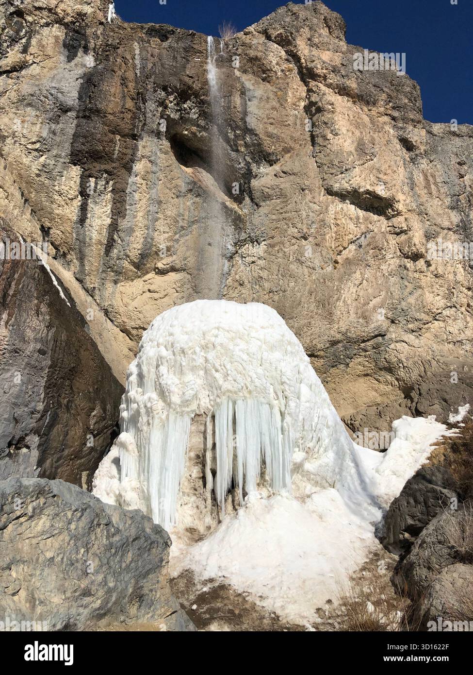 Cascata congelata di Sangan vicino a Teheran: Enorme cupola di ghiaccio e ghiaccioli appesi contro una scogliera aspra sotto un cielo invernale limpido. Foto Stock