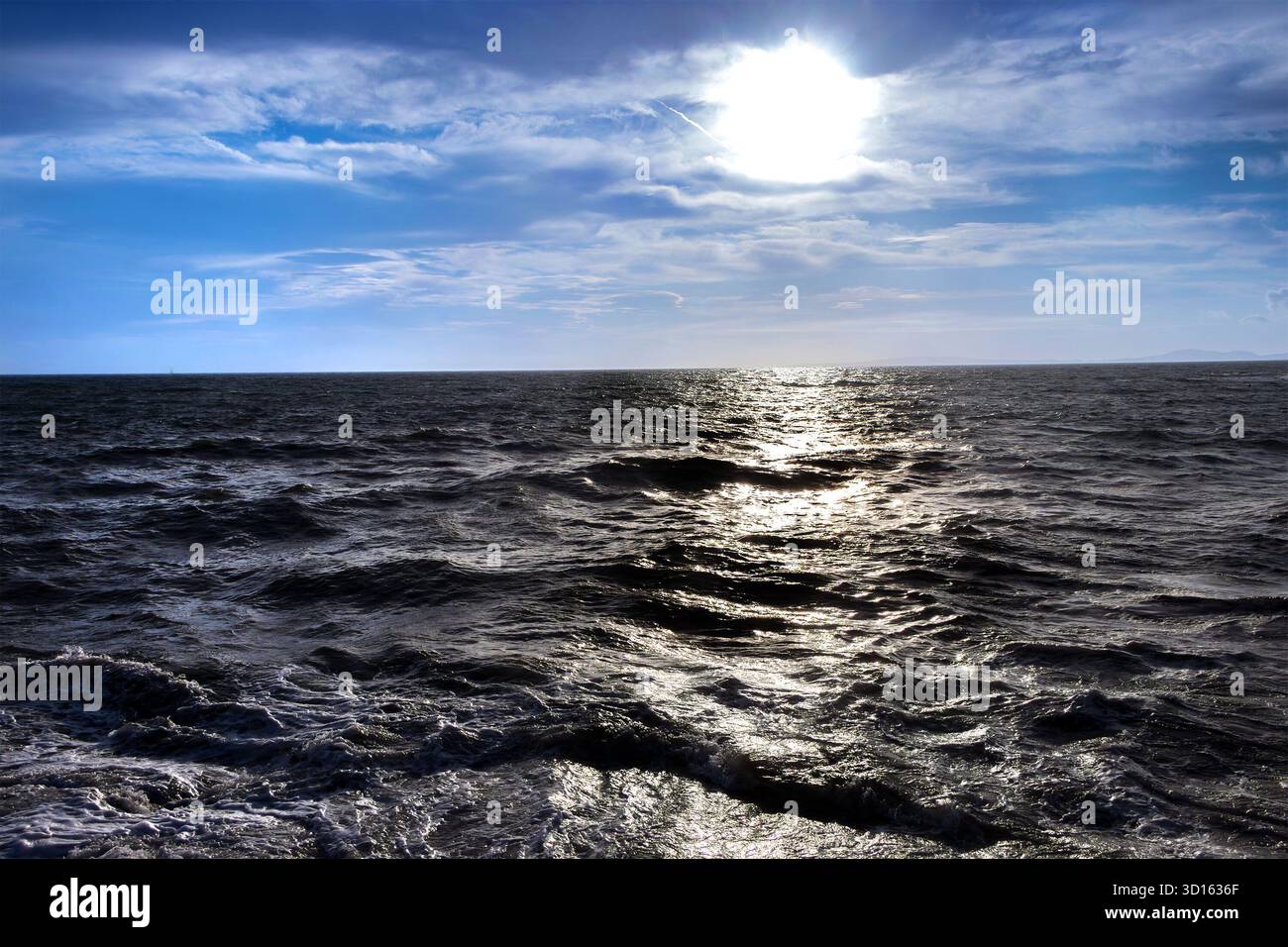 Il sole si riflette sulle scure onde ondulate dell'oceano sotto un cielo parzialmente nuvoloso nel tardo pomeriggio o nelle prime ore della sera Foto Stock
