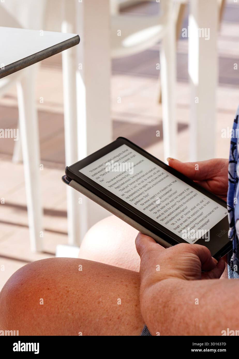 Primo piano di una donna che legge un eBook kindle su un tablet digitale mentre siede all'aperto con sedie bianche sullo sfondo c'an pastilla mallorca Foto Stock
