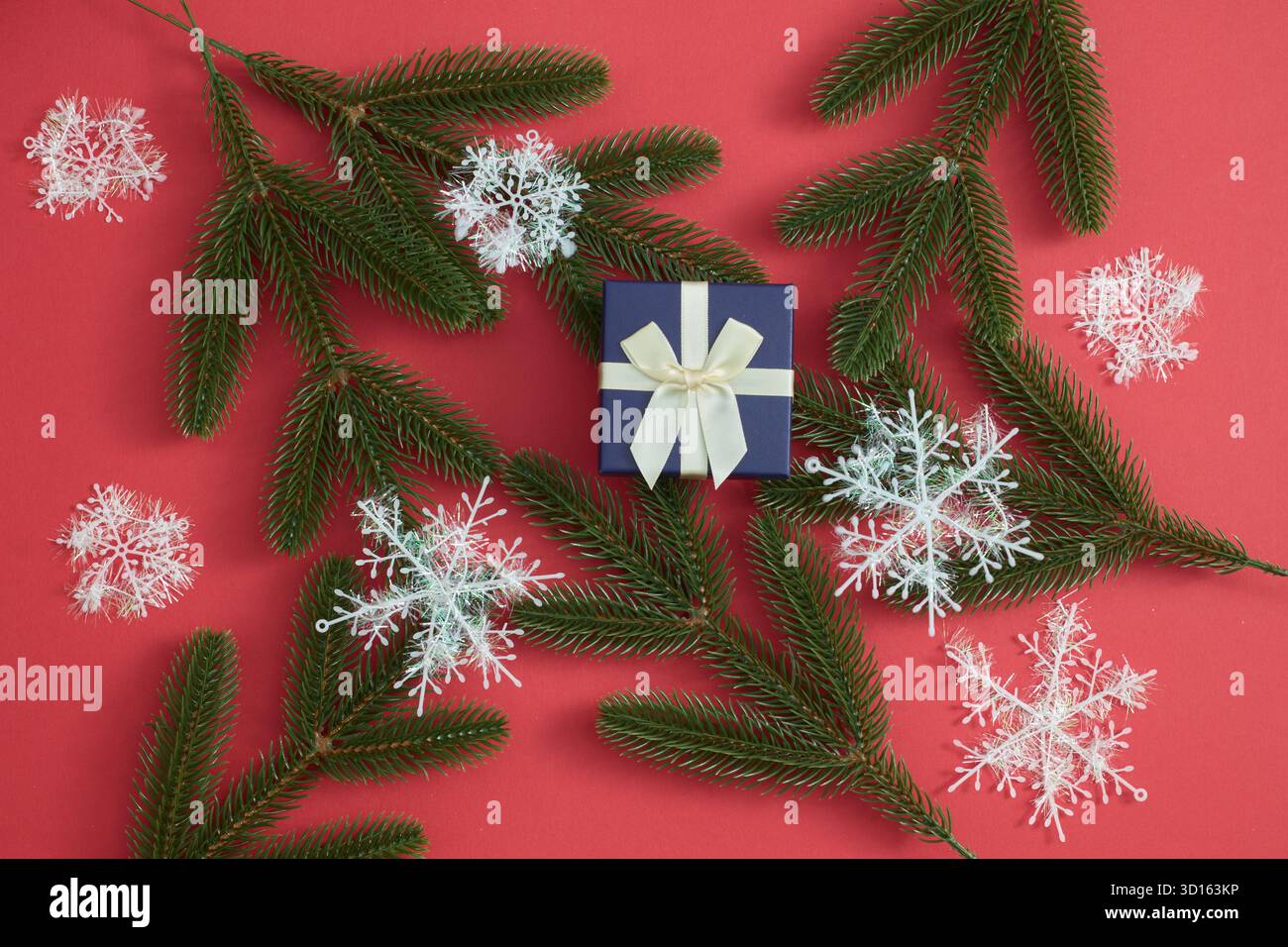 Confezione regalo, rami di abete rosso, fiocchi di neve su sfondo rosso festivo Foto Stock