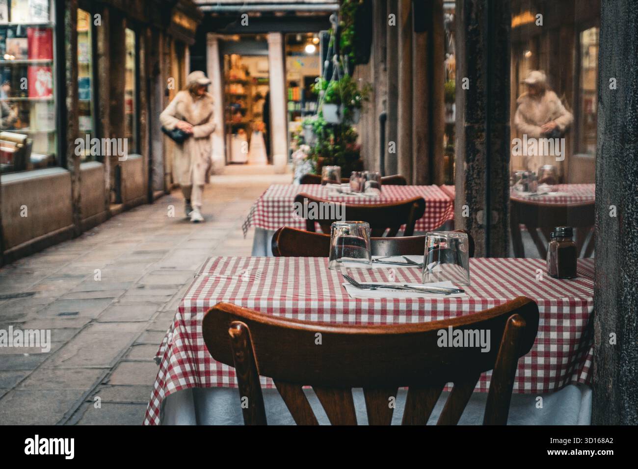 Tavoli vuoti all'aperto del ristorante con tovaglie a scacchi in uno stretto vicolo veneziano, Venezia, Italia, in una giornata nuvolosa Foto Stock