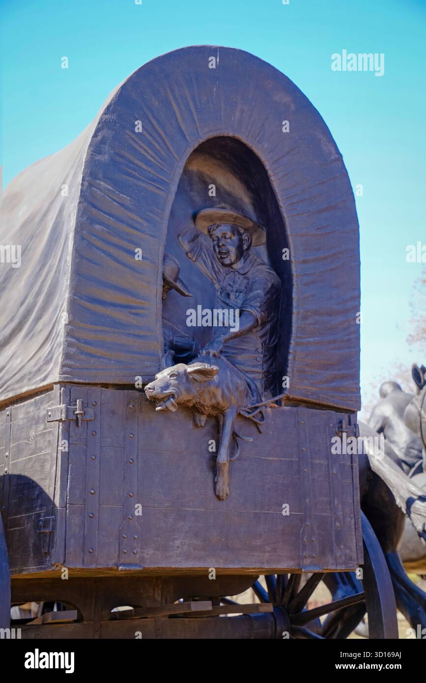 Scultura in bronzo di un pioniere che tiene in mano un cane mentre salta da un carro coperto al Centennial Land Run Monument di Bricktown Foto Stock