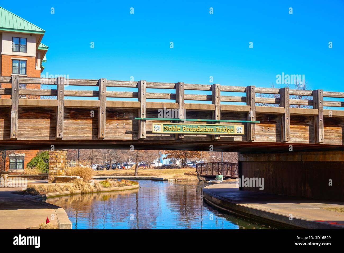 Vista del Noble Foundation Bridge sul canale di Bricktown in una giornata limpida, evidenziando la struttura in legno, l'acqua calma e il paesaggio urbano soleggiato Foto Stock