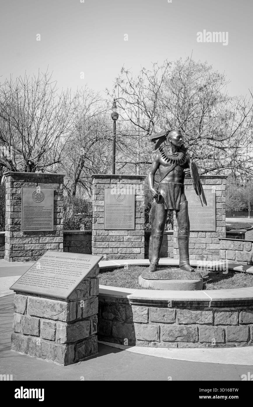 Immagine in bianco e nero della statua del guerriero Chickasaw e targhe storiche esposte vicino al canale di Bricktown, che evidenziano il patrimonio culturale e il simbolismo Foto Stock