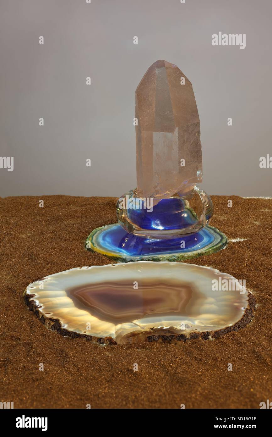 Natura morta con due fette retroilluminate di agata e cristallo di roccia su sabbia dorata. Scena illuminata da luci alogene. Foto con grande profondità di campo. Foto Stock