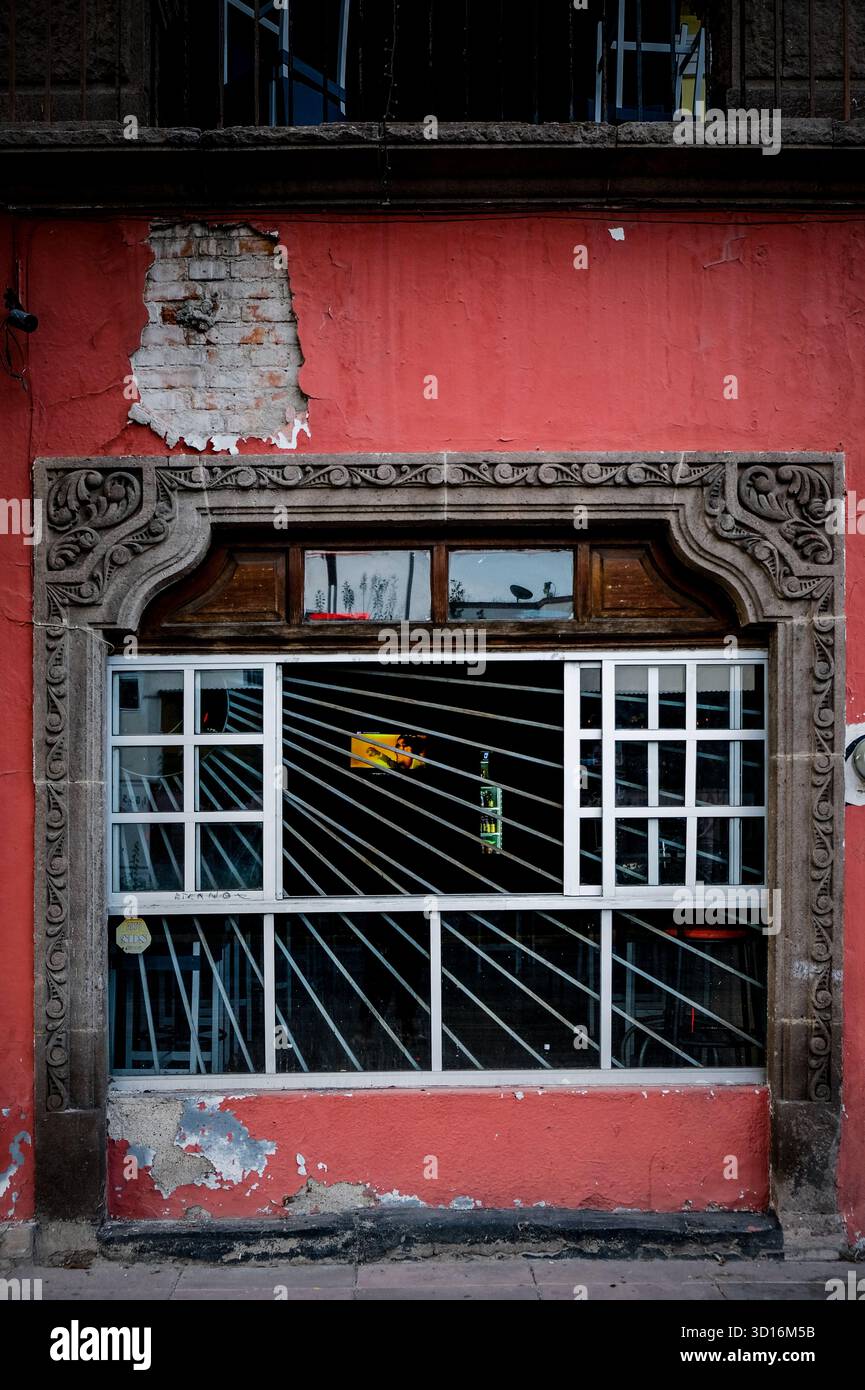 Muratura dell'edificio di colore rosso con cornice in pietra ornata e griglia in metallo barrato in uno stile architettonico tradizionale Foto Stock