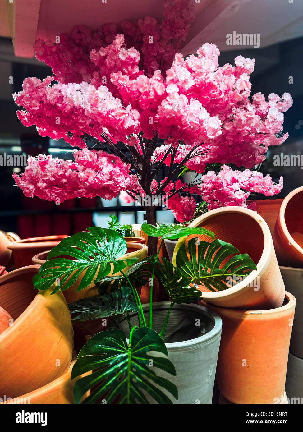 Vivace mostra di un albero di ciliegio rosa artificiale in fiore circondato da vasi di terracotta e fogliame verde artificiale. Foto Stock