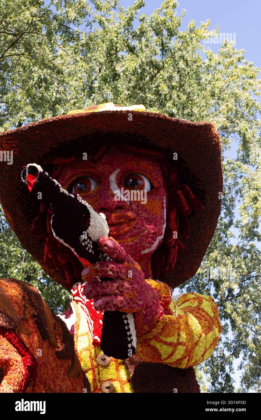 Petali dahlia rossi e gialli che coprono i bordi della trave galleggiante della parata, decorazioni a rete con corda visibile, texture a mosaico floreale all'aperto al festival olandese 2025 Foto Stock