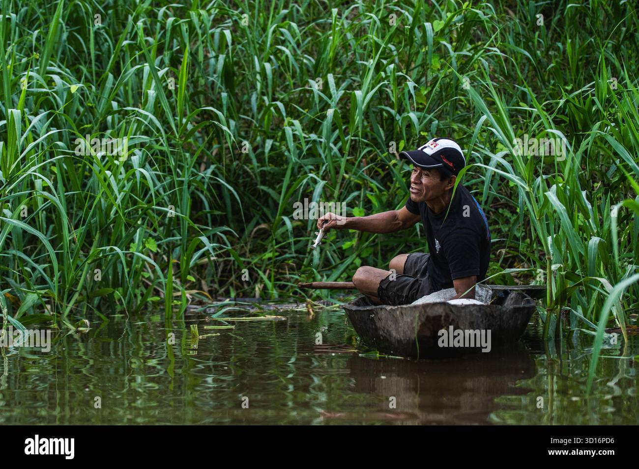 Uomo locale che cattura pesci su una tradizionale canoa in legno attraverso una fitta vegetazione su un piccolo affluente del Rio delle Amazzoni vicino a Nauta, Loreto, Perù, 2024. Foto Stock