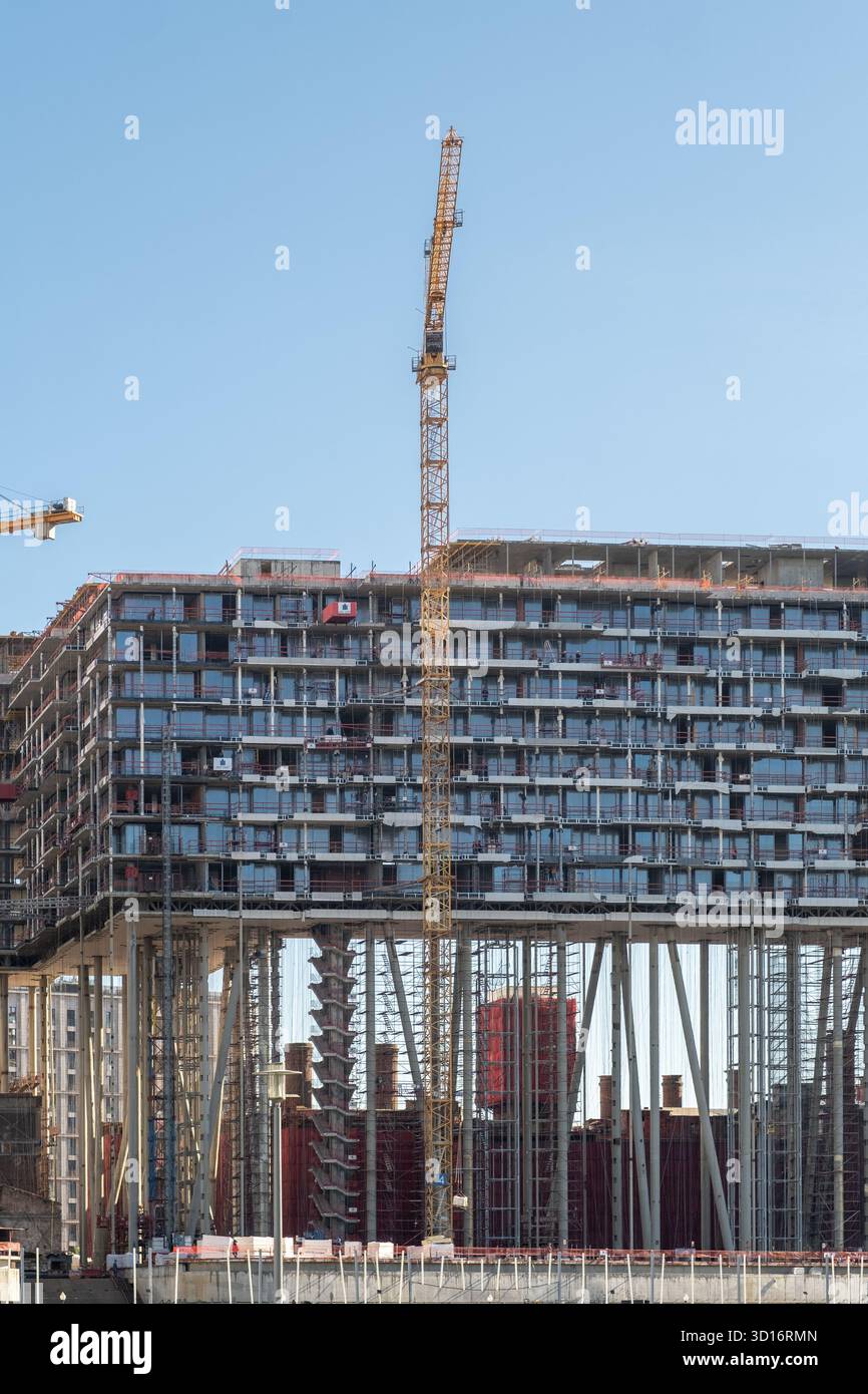 I lavoratori continuano a costruire una moderna e alta struttura che mostra gru e ponteggi, con cieli limpidi che circondano il vivace cantiere Foto Stock
