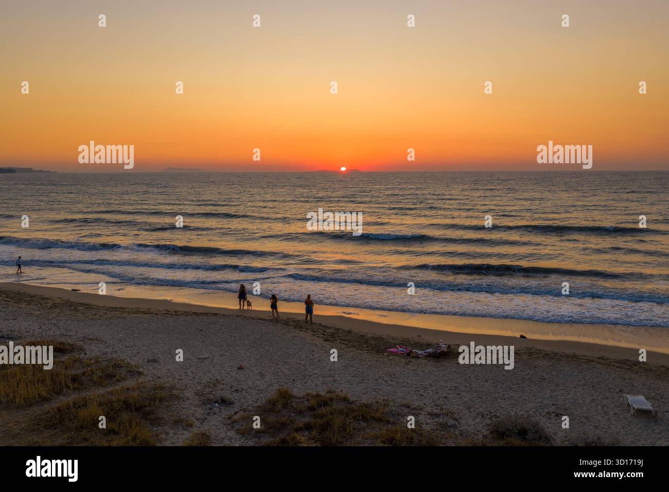 Tramonto su una splendida spiaggia di sabbia con onde che si infrangono dolcemente, creando un'atmosfera serena e romantica, perfetta per una serata rilassante in riva al mare. Foto Stock