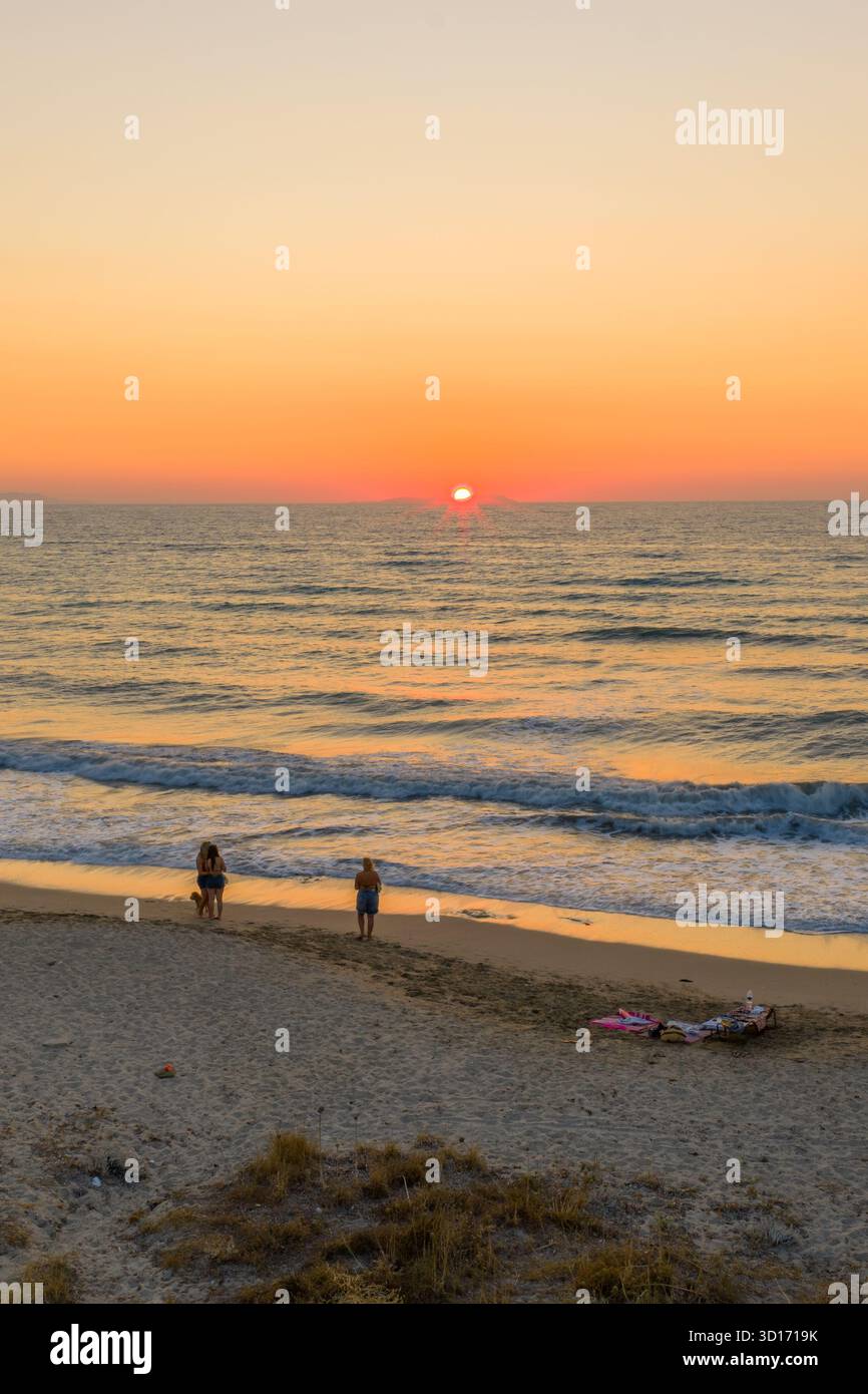Tramonto sereno su una spiaggia dorata con onde dolci, perfetto per una serata tranquilla e romantica in riva al mare, catturando la bellezza della natura e delle vacanze Foto Stock