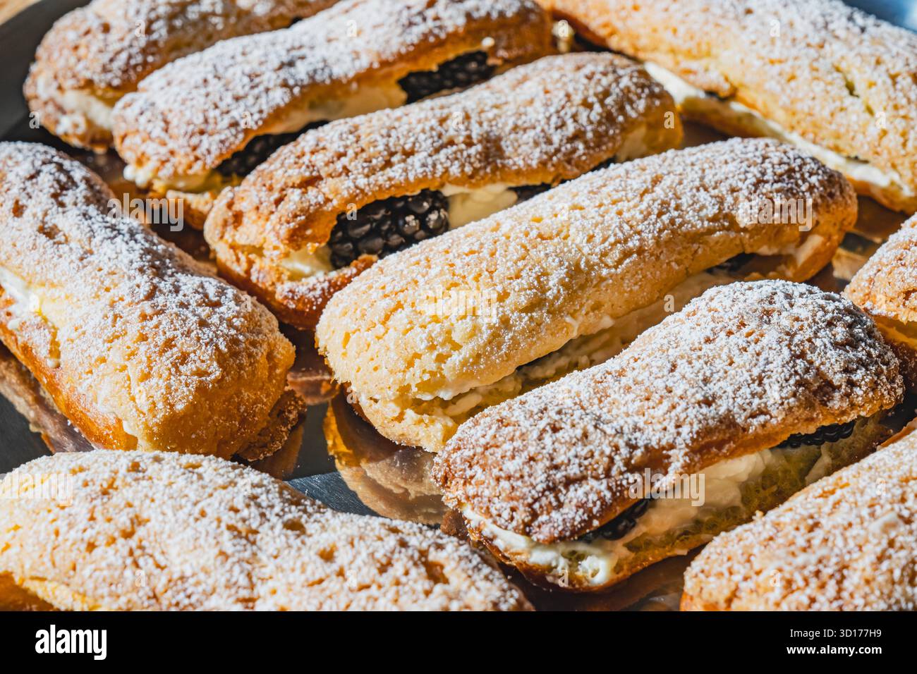 Un piatto di éclair dorati spolverati di zucchero a velo, ripieni di panna e more Foto Stock