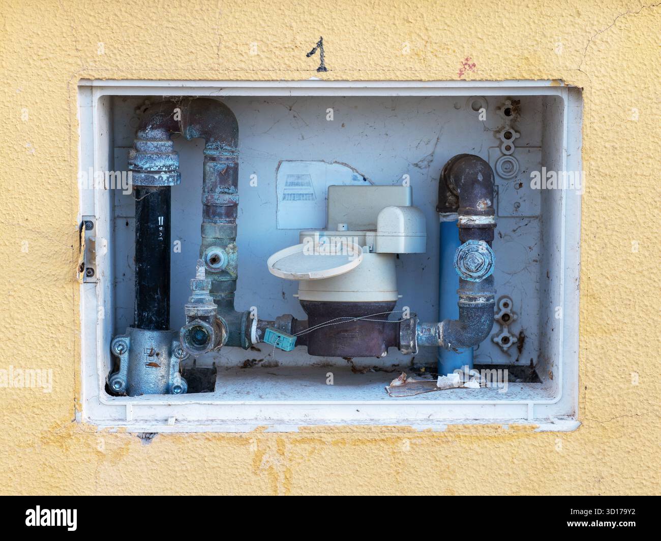 Installazione del misuratore dell'acqua integrata in una parete in stucco giallo. La scatola incassata contiene tubi, valvole e un misuratore meccanico che mostra segni di usura. Foto Stock