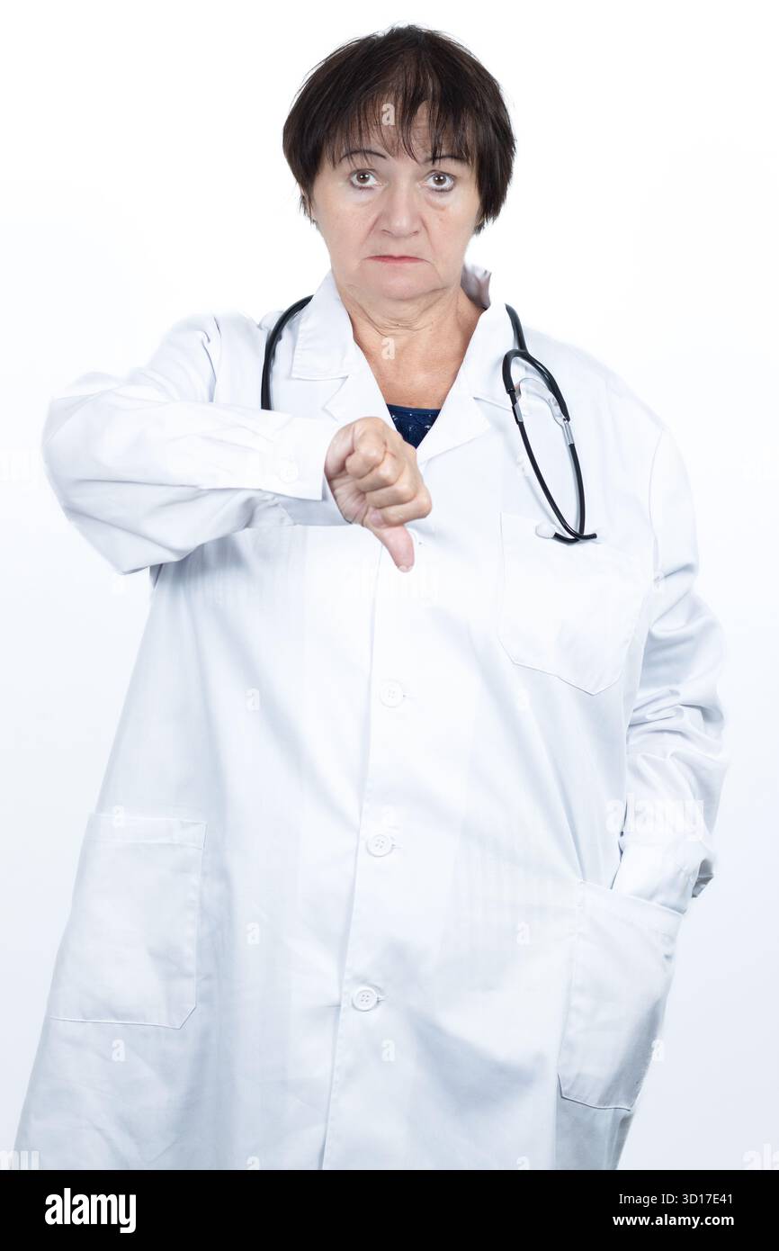 Medico donna che indossa un camice da laboratorio bianco e uno stetoscopio che mostra un gesto con il pollice rivolto verso il basso, esprimendo disapprovazione e delusione Foto Stock