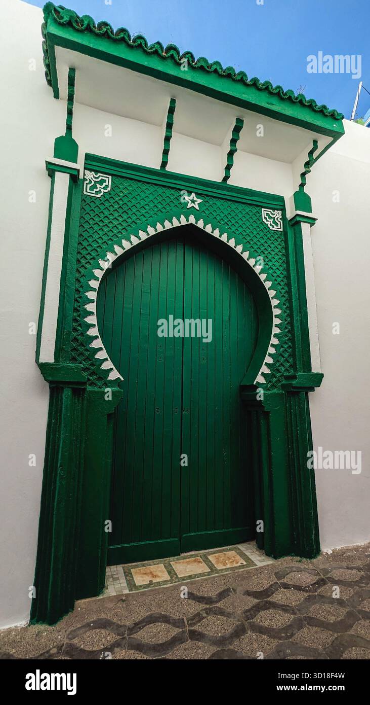 Porta ad arco verde finemente intagliata con accenti bianchi e tradizionale design marocchino su una parete in stucco bianco Foto Stock