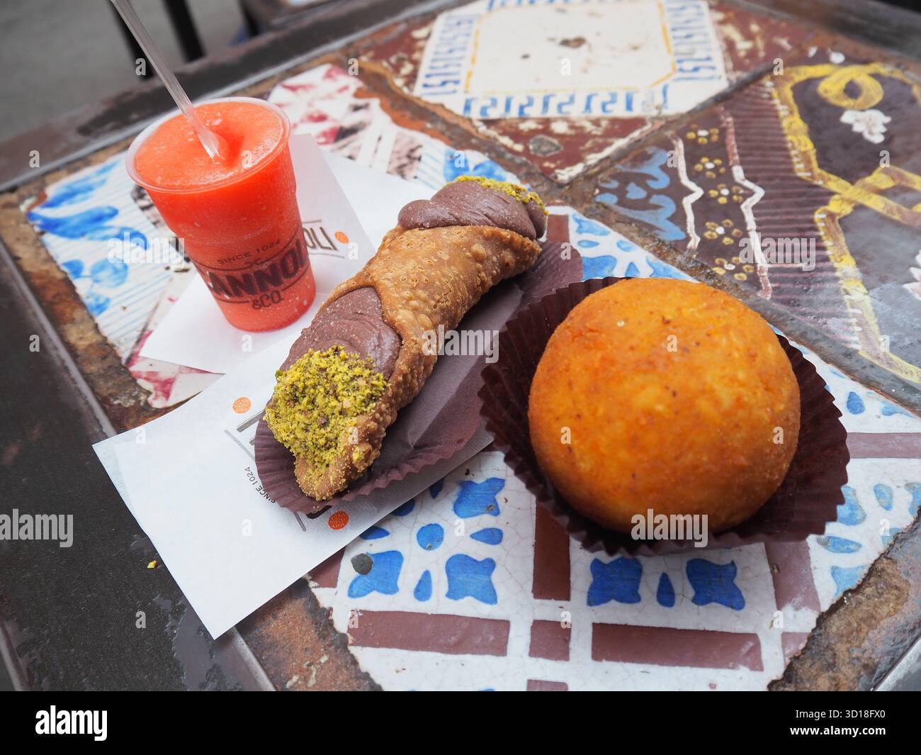 Cannolo arancini siciliani e granita di fragole su un tavolo decorato all'aperto a Palermo Foto Stock