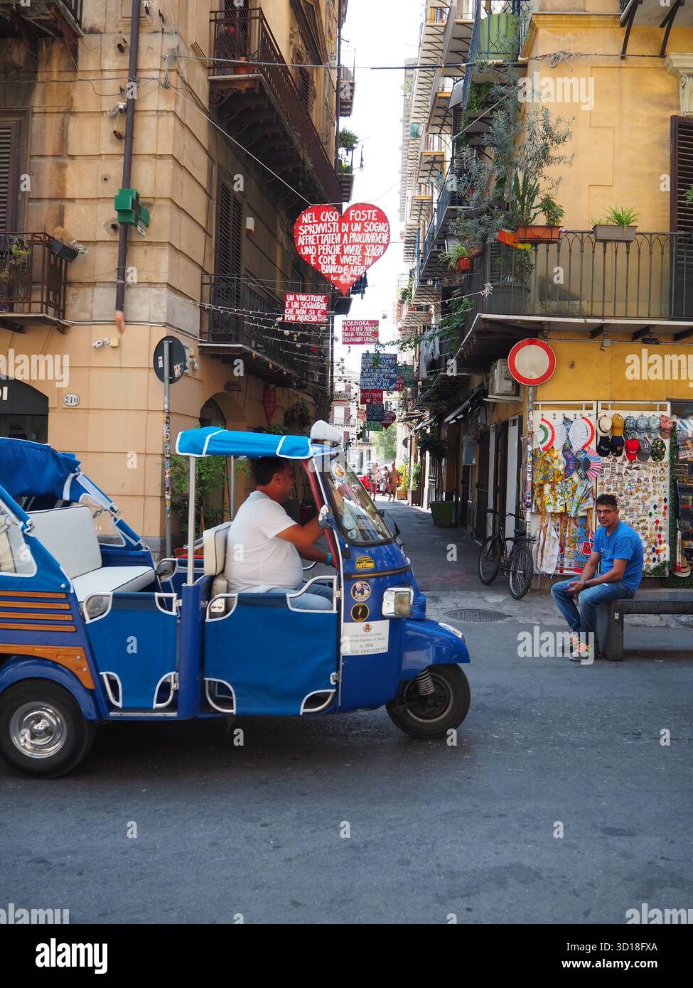 Taxi blu a tre ruote su una strada vivace con decorazioni sospese a Palermo in Sicilia Foto Stock