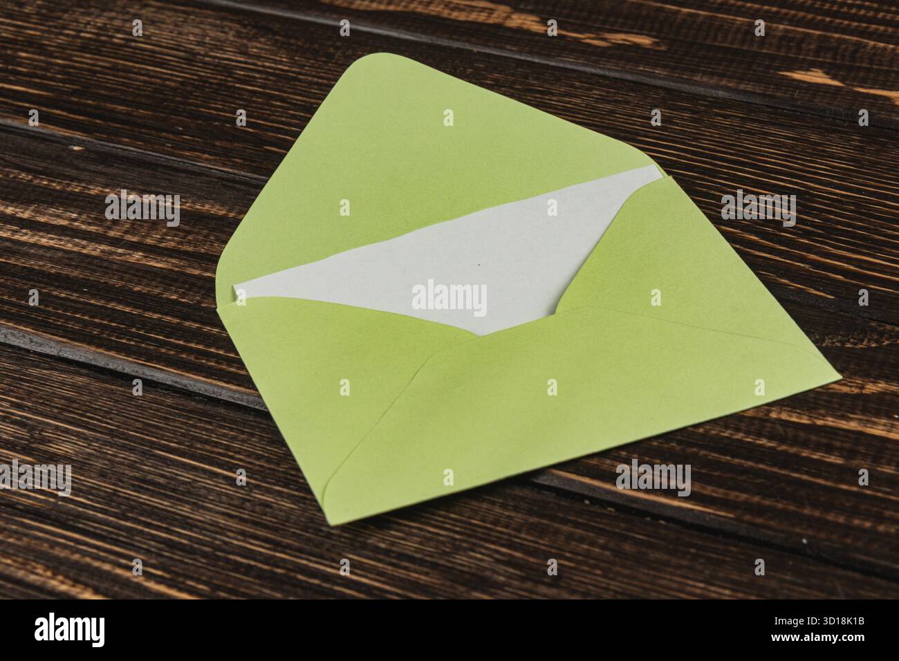 Una busta verde si trova aperta su un rustico tavolo di legno, rivelando carta bianca bianca all'interno, pronta per un messaggio o un biglietto personale. Foto Stock