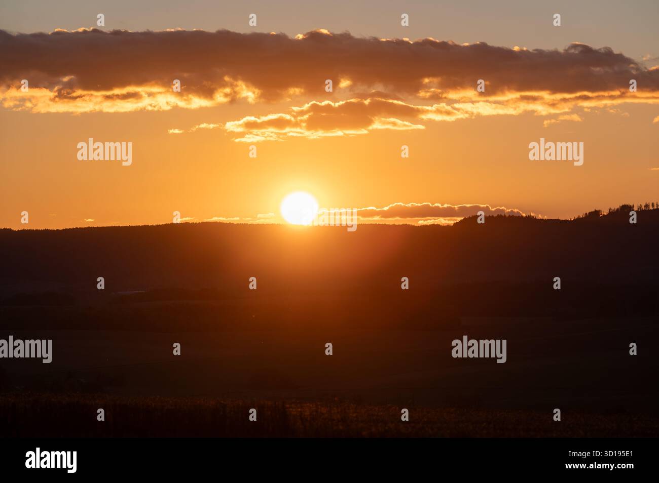 Tramonto all'orizzonte con spettacolari nuvole nel cielo, che dipingono tonalità calde di arancione, rosso e giallo nel paesaggio serale. Foto Stock